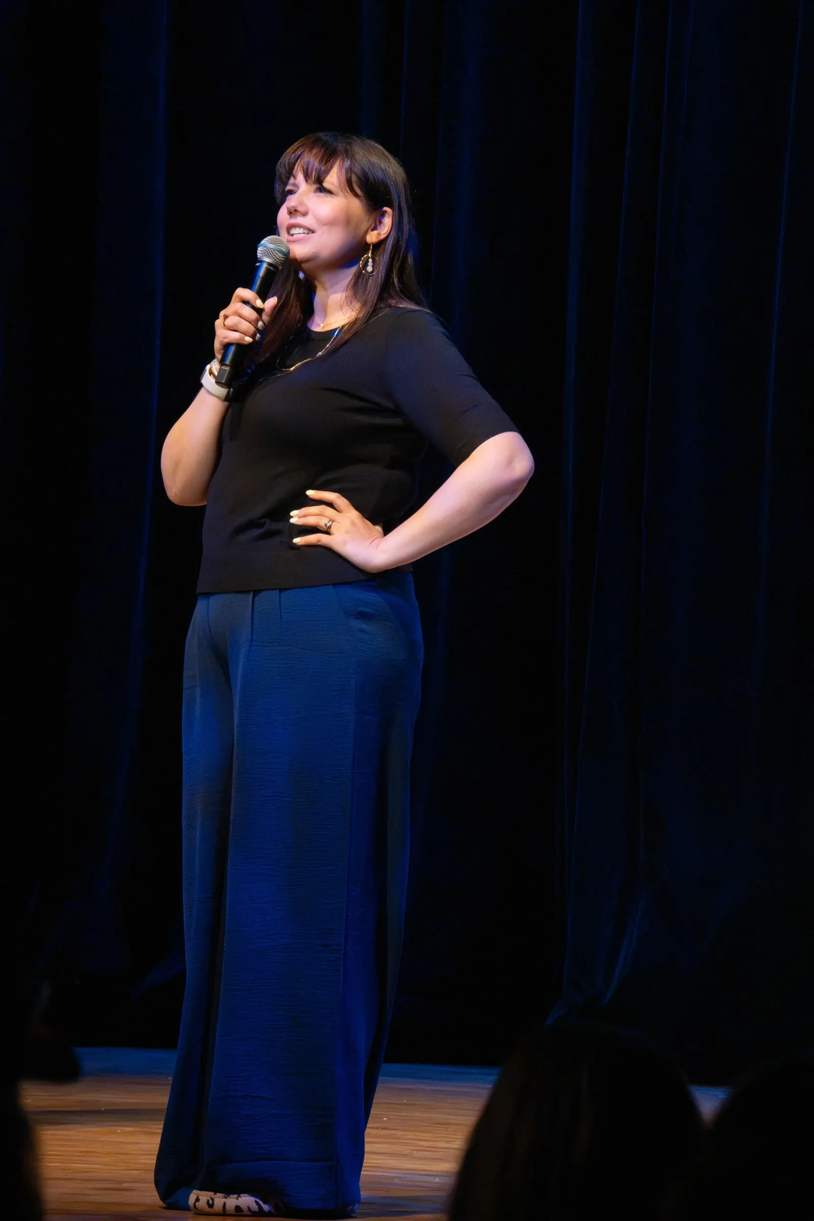 Brooke on stage, smiling, microphone in hand and one hand on her hip
