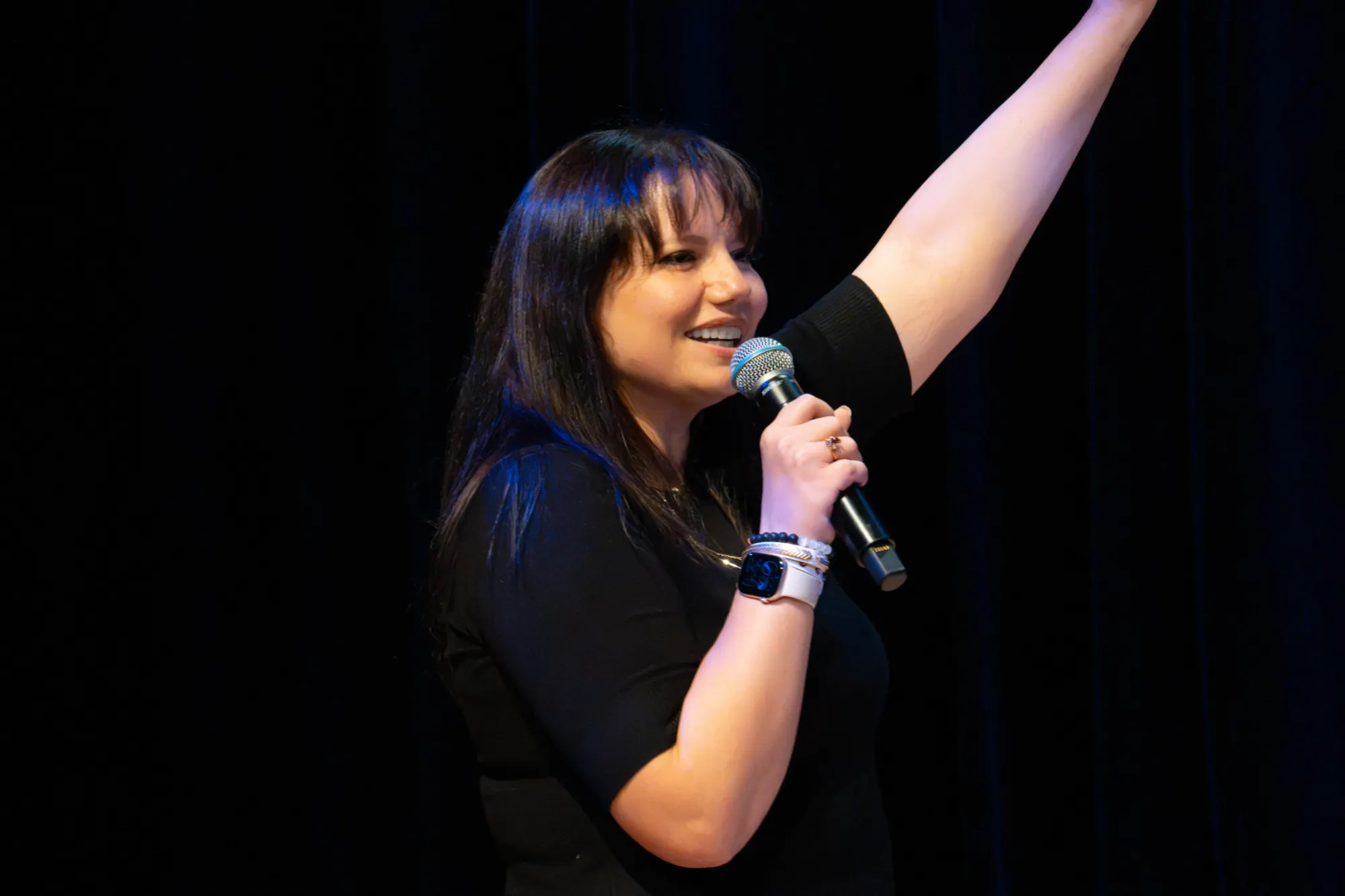 Brooke on stage, laughing, one arm in the air and a microphone in the other hand